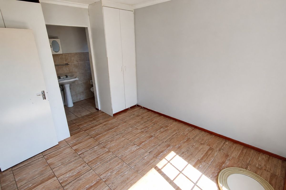 An empty bedroom featuring tiled flooring, built-in cupboards, and direct access to an en-suite bathroom with a pedestal basin and toilet.
