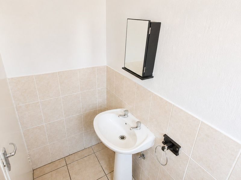 A clean, functional bathroom featuring a pedestal basin, tiled splashback, and a wall-mounted mirror cabinet.