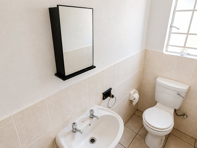 A functional guest bathroom featuring a ceramic basin, toilet, and wall-mounted mirror cabinet with neutral tiled finishes.
