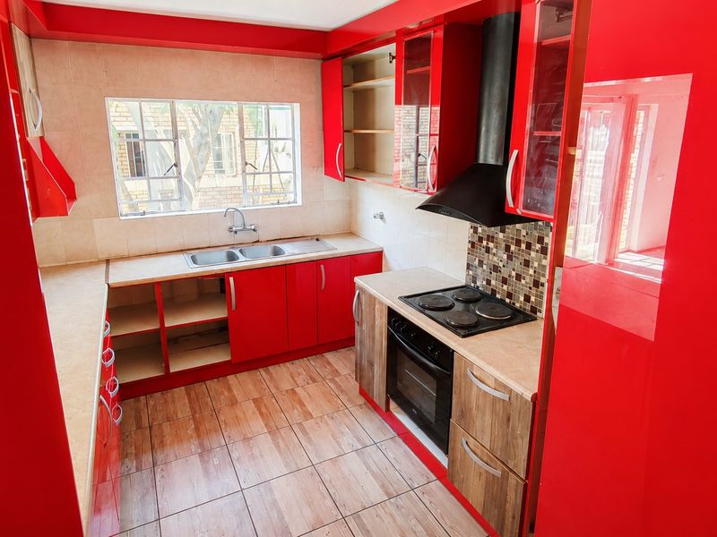 A kitchen featuring red cabinetry, a built-in oven and hob, and a double basin sink. The space is currently vacant and requires cosmetic updates.