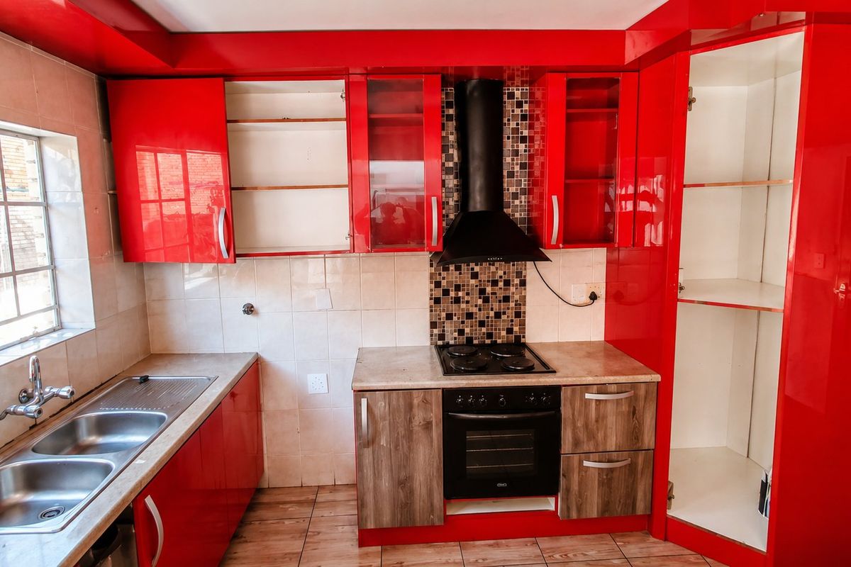 A kitchen featuring red and wood-tone cabinetry, a double basin sink, and built-in cooking appliances with a tiled splashback and flooring.
