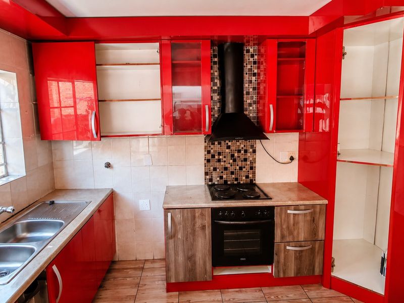 A kitchen featuring red and wood-tone cabinetry, a double basin sink, and built-in cooking appliances with a tiled splashback and flooring.