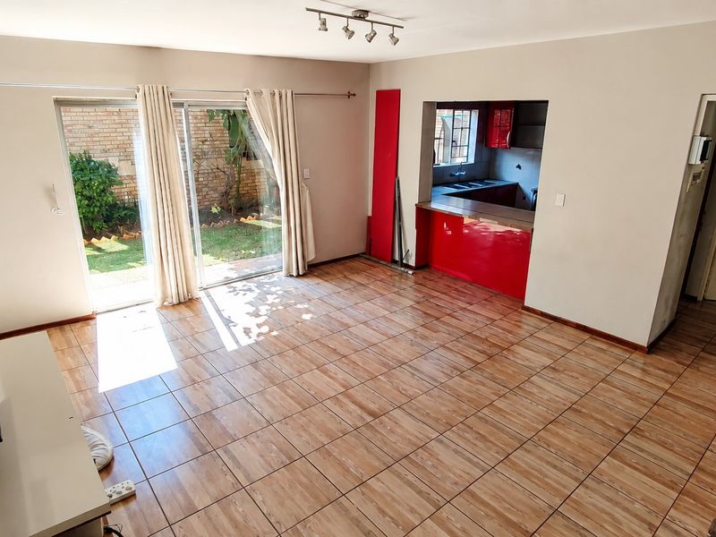 Open plan living area featuring tiled floors, a sliding door to the garden, and a kitchen pass-through with red cabinetry.