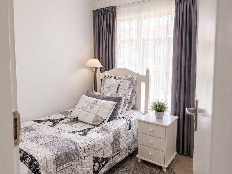 A compact bedroom featuring tiled flooring and large windows with fitted curtains, offering a bright and functional living space.