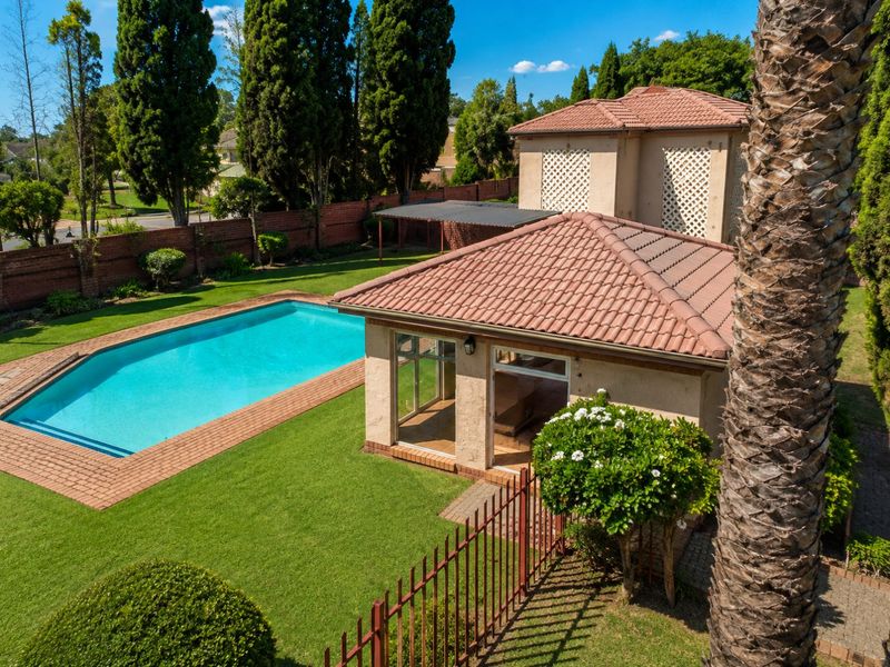 Aerial view of a well-maintained backyard featuring a swimming pool, paved surround, lush lawn, and a detached structure with a tiled roof.