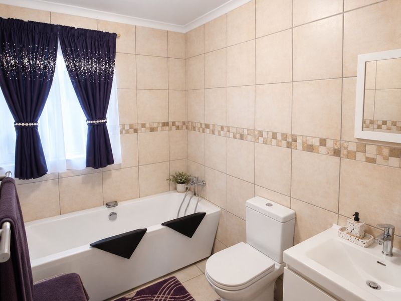 A functional bathroom featuring a bathtub, toilet, and vanity basin with neutral wall tiling and a decorative mosaic border.
