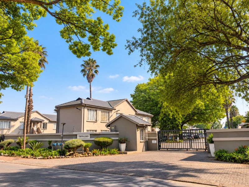 Front entrance view of Theda Oaks apartment complex featuring a secure gated access point, perimeter walling, and paved driveway.