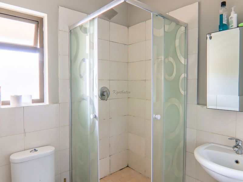 A functional bathroom featuring a shower enclosure, pedestal washbasin, toilet, and mirror cabinet with neutral wall tiling.