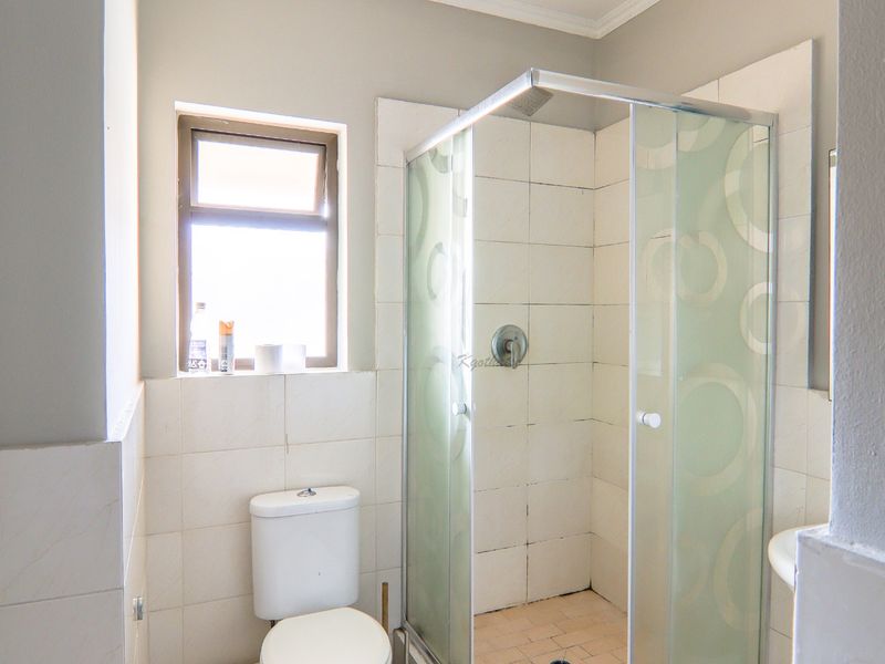 A functional bathroom featuring a glass shower enclosure, a standard toilet, and tiled finishes, offering a clean and practical space.