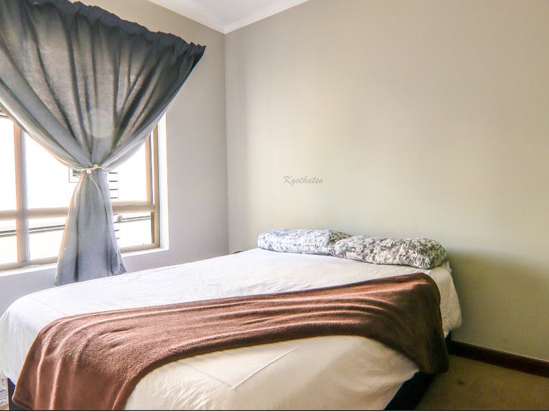 A bedroom featuring neutral wall finishes, a built-in wardrobe, and an aluminium-framed window allowing natural light.