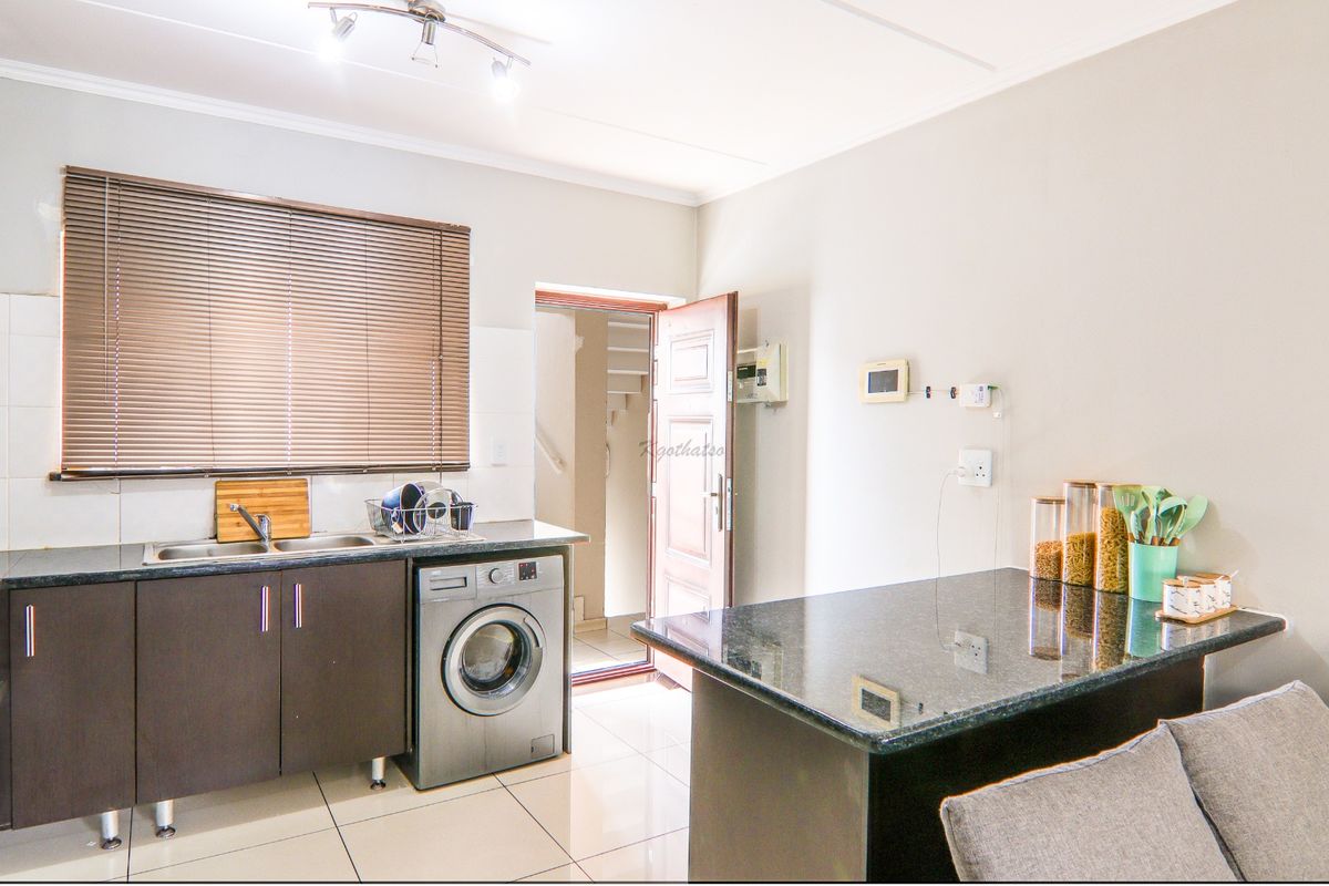 A functional kitchen featuring dark cabinetry, granite countertops, a breakfast bar, and tiled flooring, with an integrated washing machine and direct outdoor access.