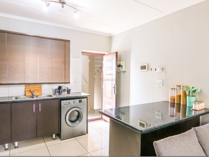 A functional kitchen featuring dark cabinetry, granite countertops, a breakfast bar, and tiled flooring, with an integrated washing machine and direct outdoor access.