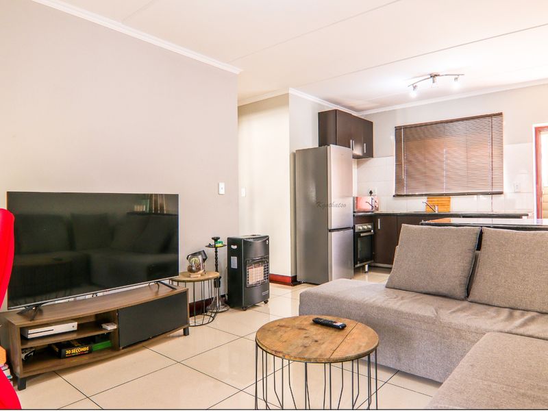 Open-plan living area featuring tiled floors and a functional kitchen with built-in cabinetry, oven, and hob, seamlessly connected to the lounge space.