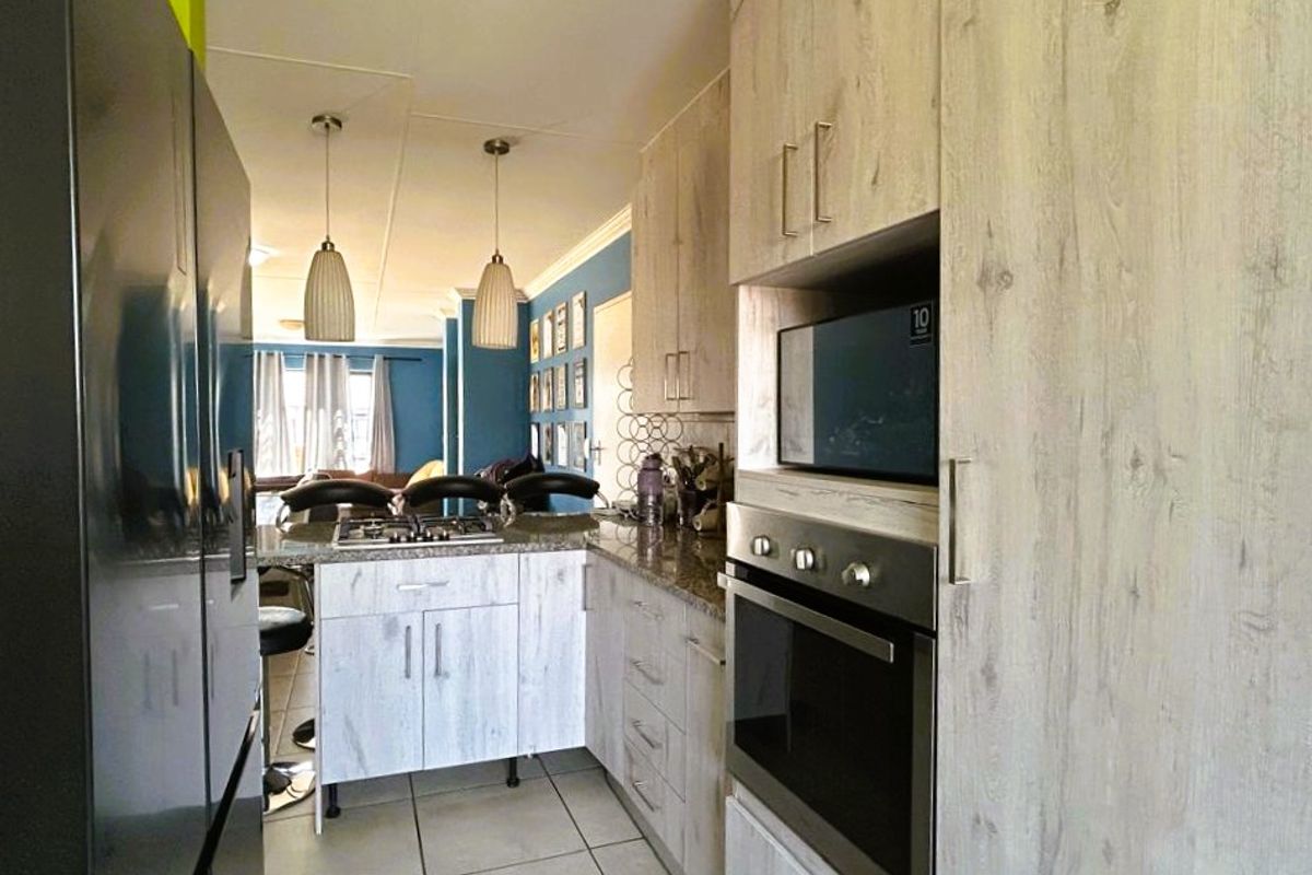 A functional kitchen featuring light wood-grain cabinetry, granite countertops, a built-in oven, and a gas hob, flowing into an open-plan living area.
