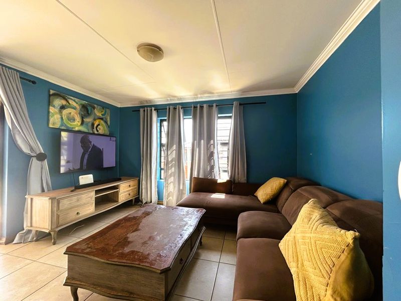 A comfortable living room featuring tiled flooring, decorative ceiling cornicing, and blue accent walls, providing a functional space for relaxation.