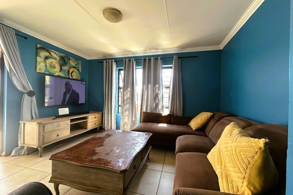 A comfortable living room featuring tiled flooring, decorative ceiling cornicing, and a central ceiling light fixture.