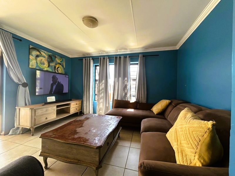A comfortable living room featuring tiled flooring, decorative ceiling cornicing, and a central ceiling light fixture.