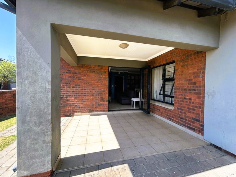A covered patio area featuring tiled flooring and exposed brick walls, providing a seamless transition to the interior living space through sliding glass doors.
