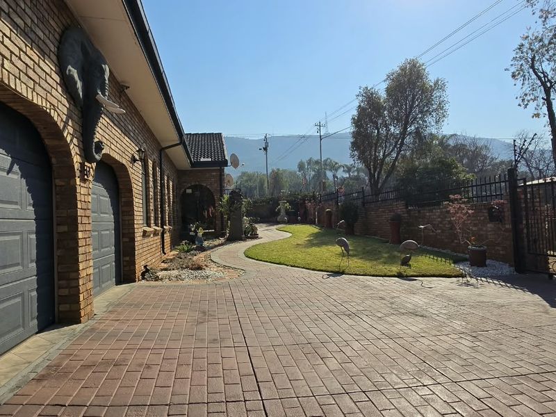 Front exterior view featuring a paved driveway, double garage, and well-maintained garden with brick facade and secure perimeter fencing.