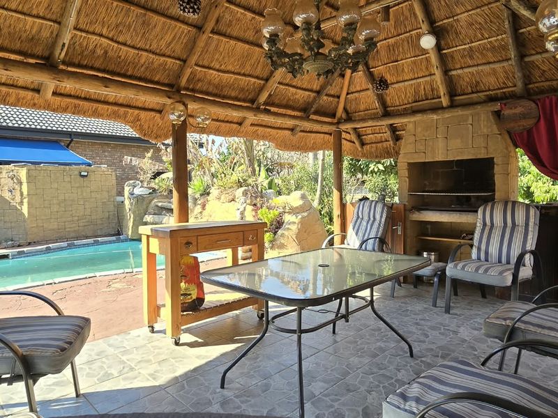 Covered outdoor patio featuring a traditional thatched roof, built-in braai with stone cladding, and direct access to the swimming pool area.