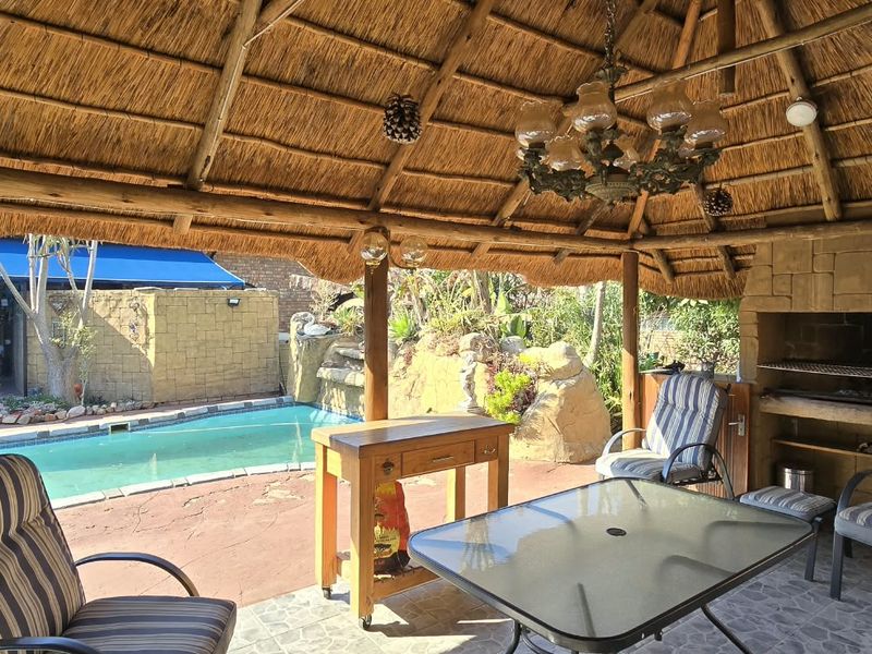 Covered outdoor entertainment area featuring a traditional thatched roof, built-in braai, and direct access to a swimming pool.