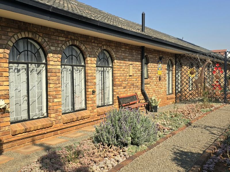 A well-maintained rear exterior view featuring a classic face brick facade, arched windows with security bars, and a landscaped gravel garden path.