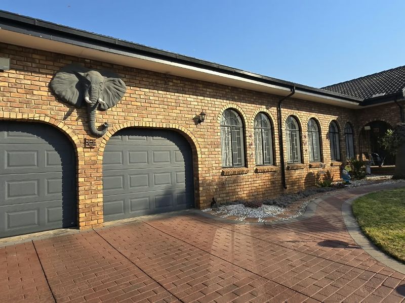 Front elevation of a face brick house featuring a double garage, arched windows, and a paved driveway.