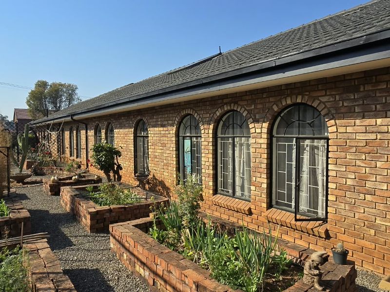 Rear exterior view of a face brick house featuring arched windows, security bars, and established raised brick garden beds.