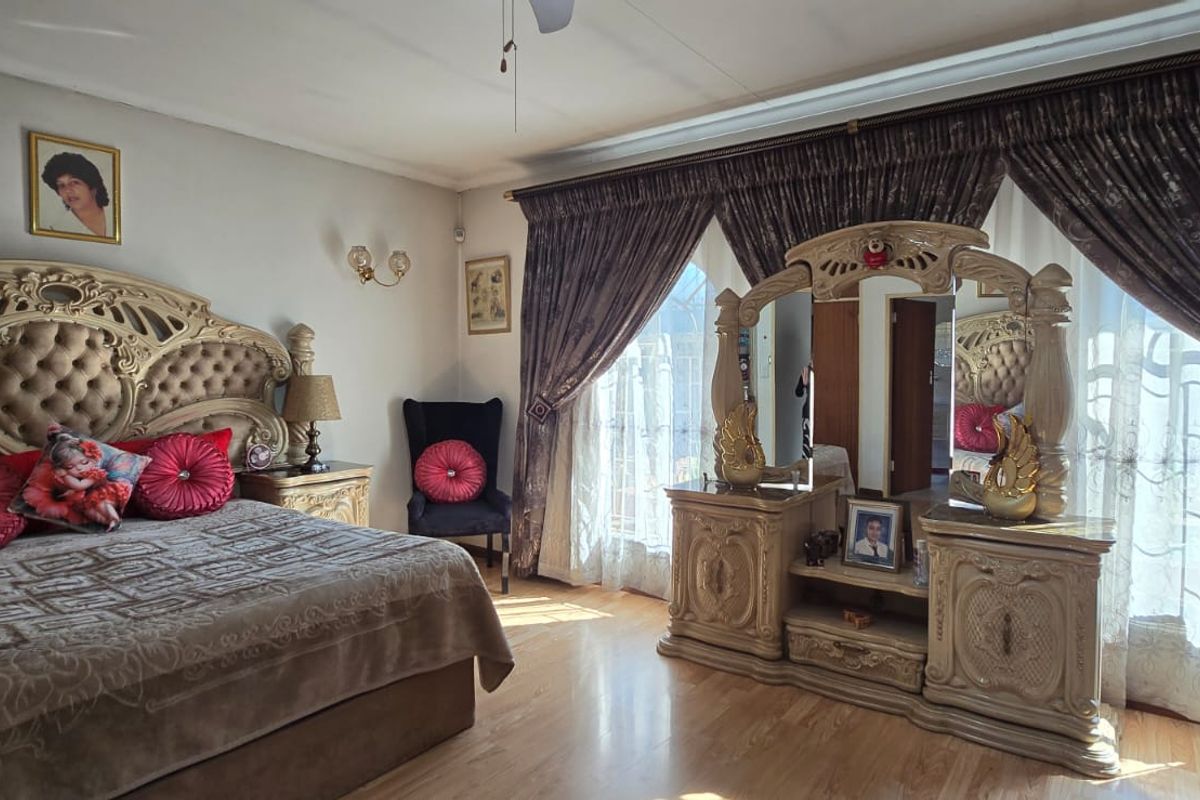 Spacious bedroom featuring laminate flooring, a ceiling fan, and large windows dressed with heavy curtains, providing ample natural light.