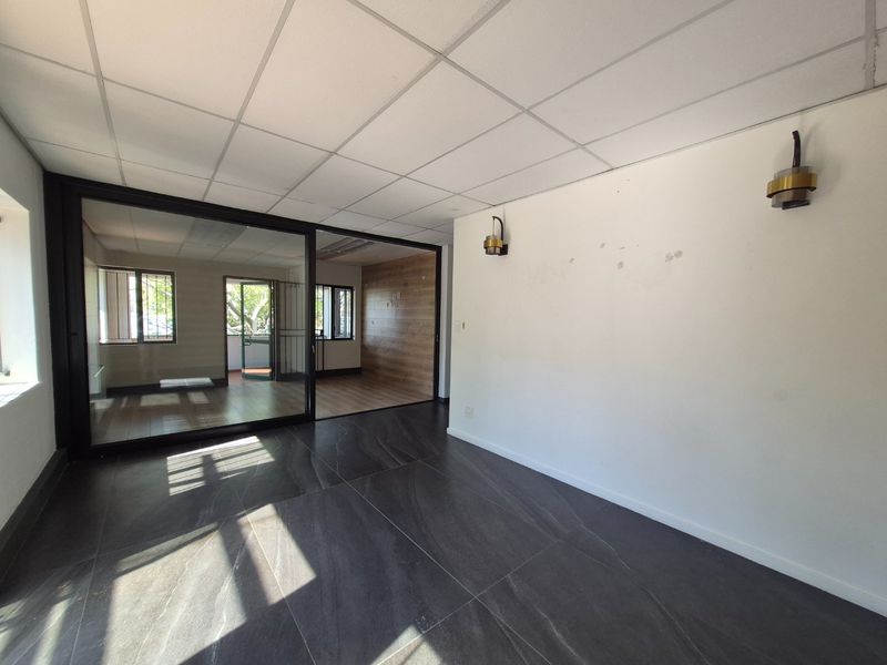 An empty commercial office space featuring a modern sliding glass partition, tiled flooring, and wall-mounted lighting fixtures.