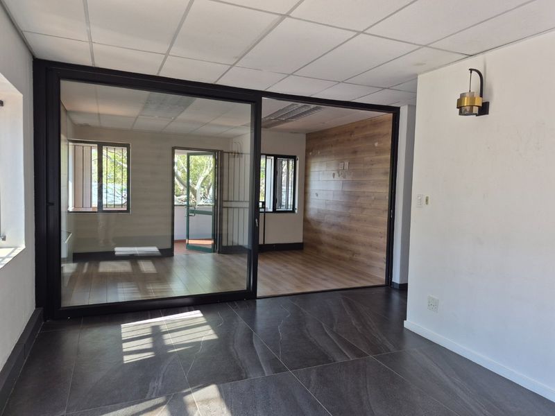 Modern commercial office space featuring a sliding glass partition, wood-look wall paneling, and a combination of dark tile and laminate flooring.