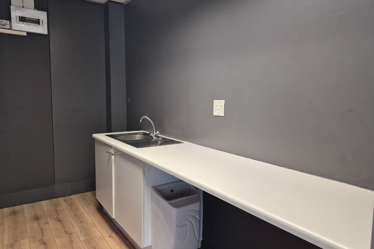 A compact kitchenette area featuring a sink, white countertop, and dark grey walls, suitable for office or utility use.