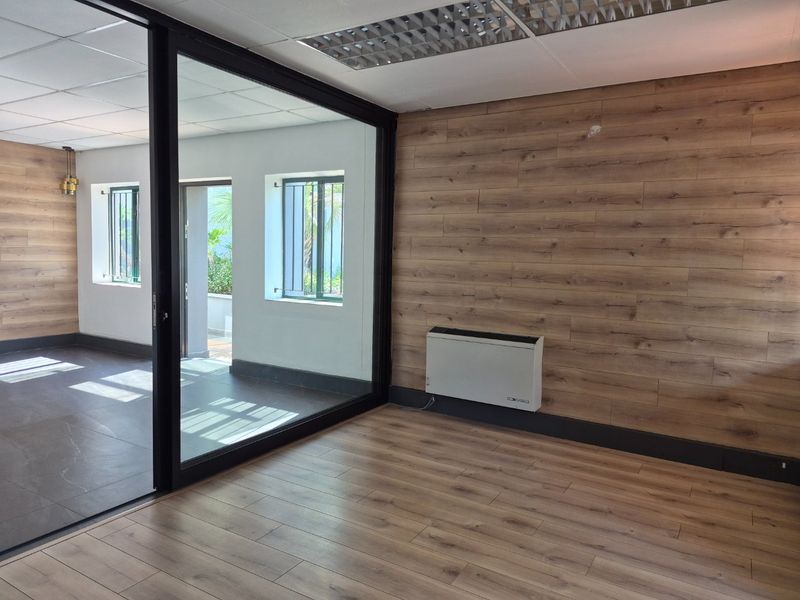 Modern office space featuring wood-look wall paneling, laminate flooring, a glass partition wall, and a wall-mounted heater.