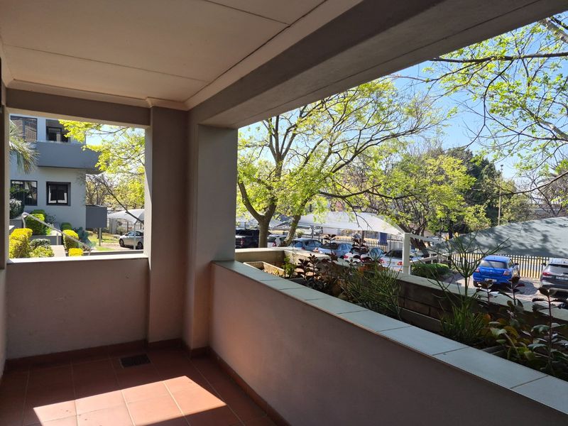 A covered balcony featuring tiled flooring and a built-in planter box, offering an open view of the surrounding commercial property grounds and parking area.