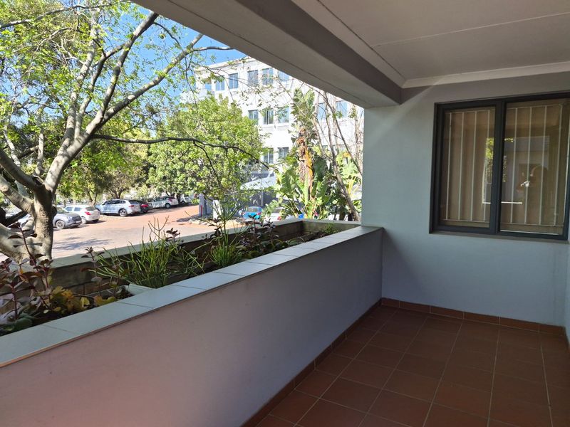 A covered balcony featuring tiled flooring and a built-in planter box, offering an outdoor space with views of the surrounding commercial area.
