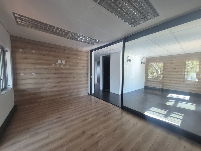Modern commercial office space featuring wood-look laminate flooring, wall paneling, and a glass partition wall with recessed lighting.