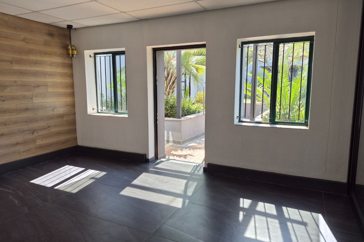 A bright, empty office space featuring modern dark tiled flooring, wood-look accent wall paneling, and direct access to an outdoor area.