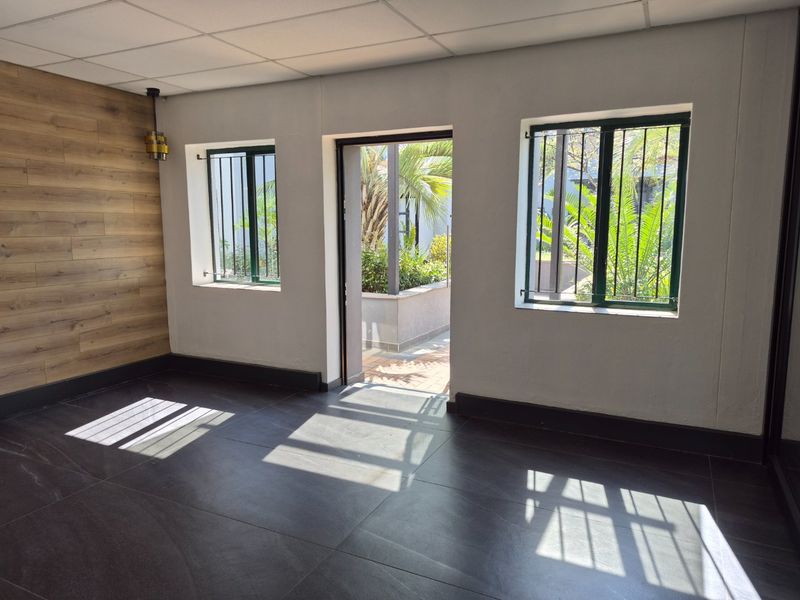 A bright, empty office space featuring modern dark tiled flooring, wood-look accent wall paneling, and direct access to an outdoor area.