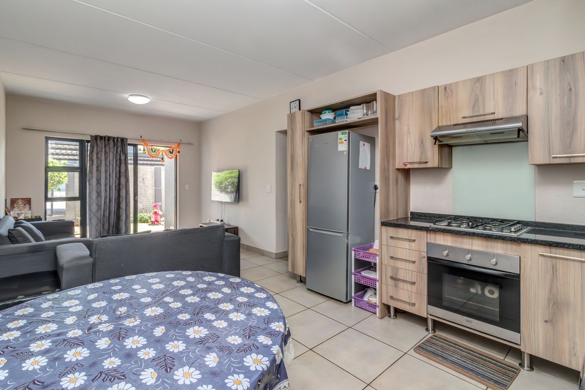 Open-plan living area featuring a modern kitchen with wood-finish cabinetry, gas hob, and oven, flowing into a lounge space with access to the patio.
