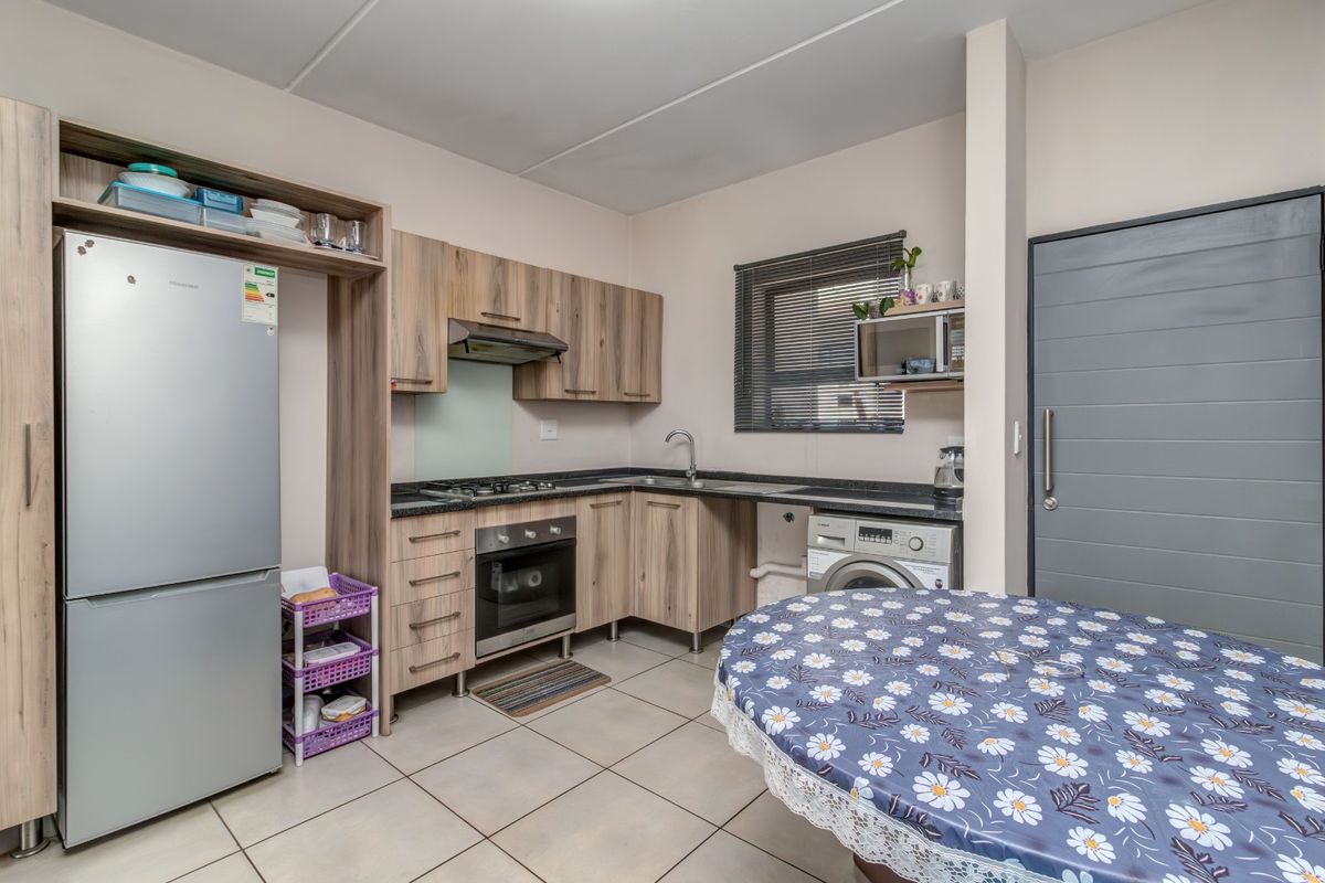 A functional kitchen featuring wood-look cabinetry, dark countertops, integrated gas hob and oven, and tiled flooring with space for laundry appliances.
