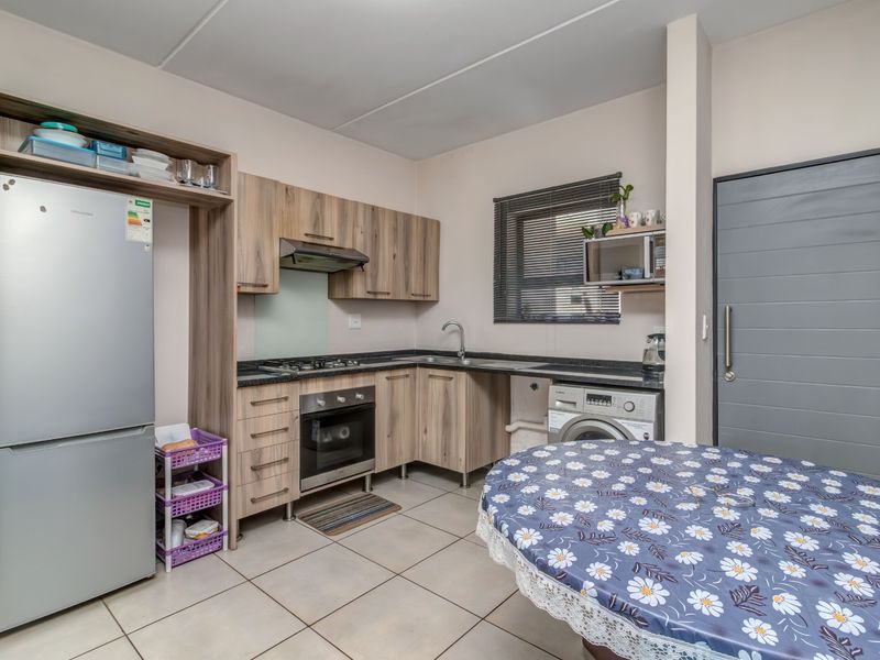 A functional kitchen featuring wood-look cabinetry, dark countertops, integrated gas hob and oven, and tiled flooring with space for laundry appliances.