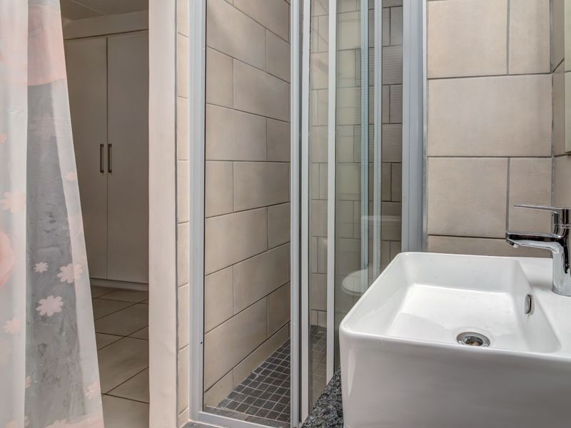 A modern bathroom featuring a vessel sink with a chrome mixer tap, granite vanity top, and a glass-enclosed shower with neutral wall tiling.