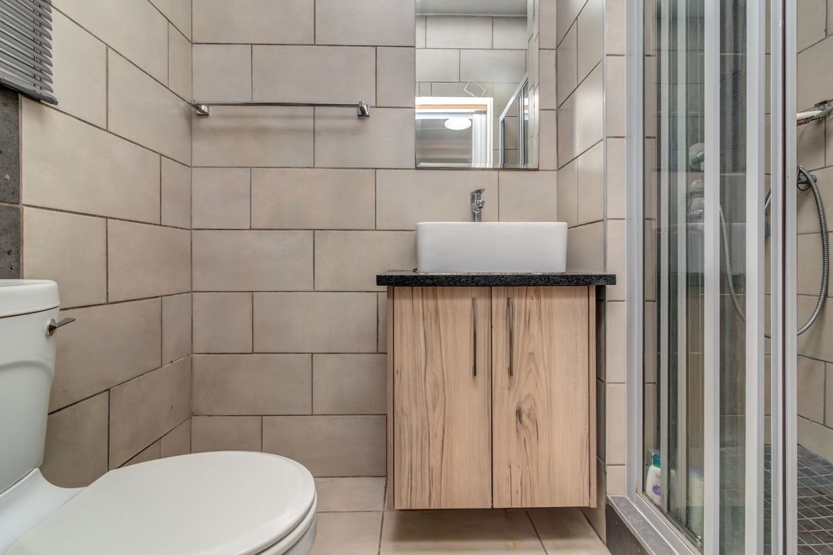 A modern bathroom featuring a wall-mounted vanity with a vessel sink, a glass shower enclosure, and neutral wall tiling.