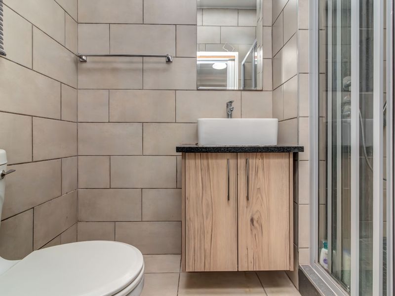 A modern bathroom featuring a wall-mounted vanity with a vessel sink, a glass shower enclosure, and neutral wall tiling.