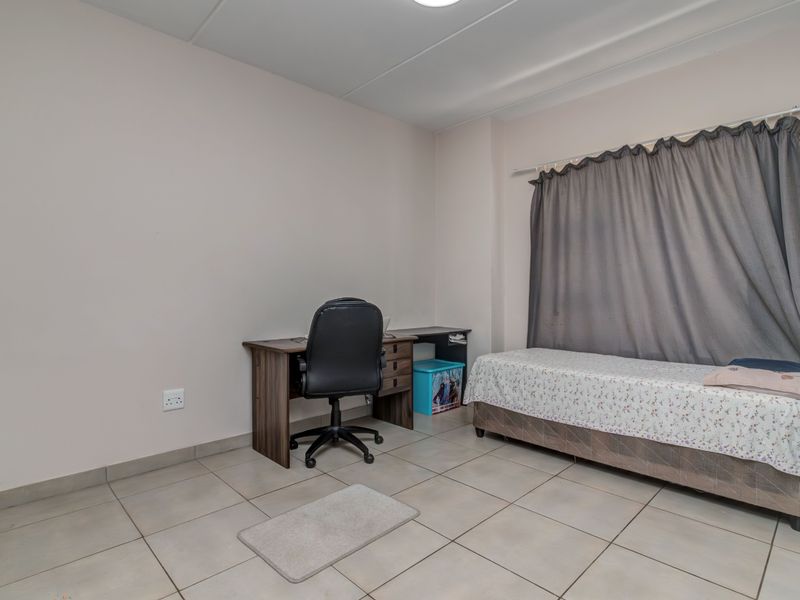A functional bedroom featuring neutral wall tones, tiled flooring, and a curtain rail, offering a clean and simple space.