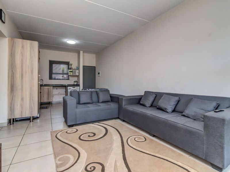 Open plan living area featuring tiled flooring and a compact kitchen corner with built-in cabinetry and sink.