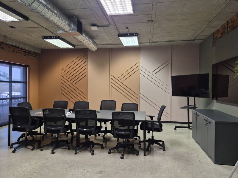 Modern commercial office boardroom featuring exposed concrete ceilings, industrial ducting, polished concrete floors, and stylish decorative wall paneling.