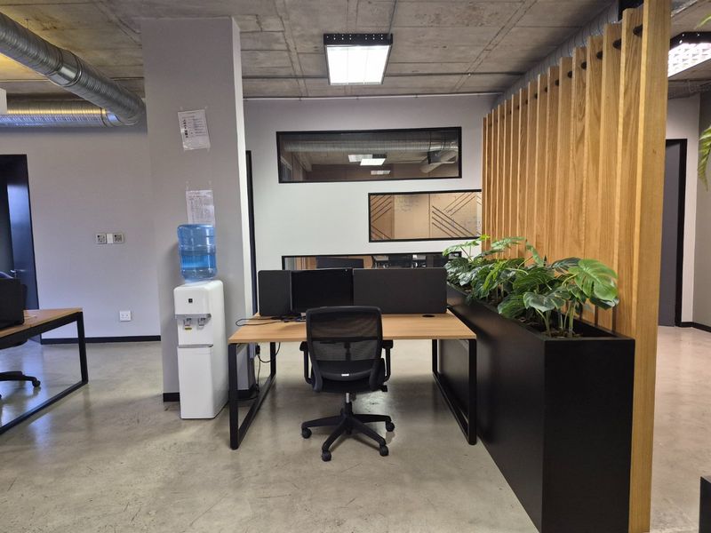 Modern open-plan office space featuring exposed concrete ceilings, industrial ducting, polished concrete floors, and a decorative timber slat partition wall.
