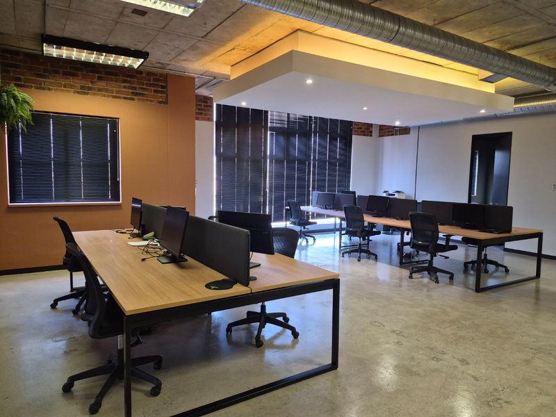 Modern open-plan office space featuring industrial design elements including exposed concrete ceilings, brickwork, and polished concrete floors with integrated lighting.
