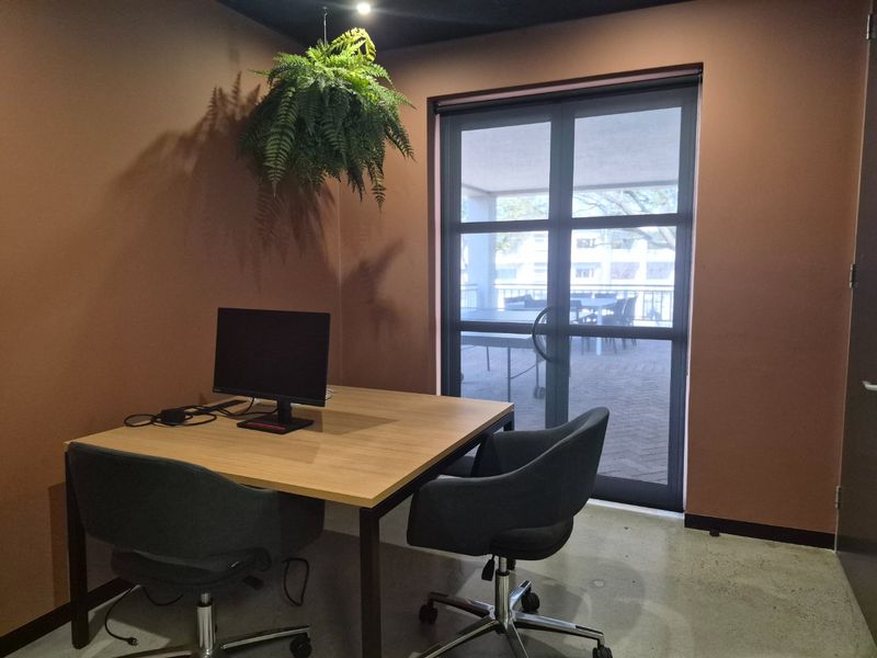 A modern office space featuring polished concrete flooring, dark accent walls, and a glass sliding door providing access to an outdoor patio area.